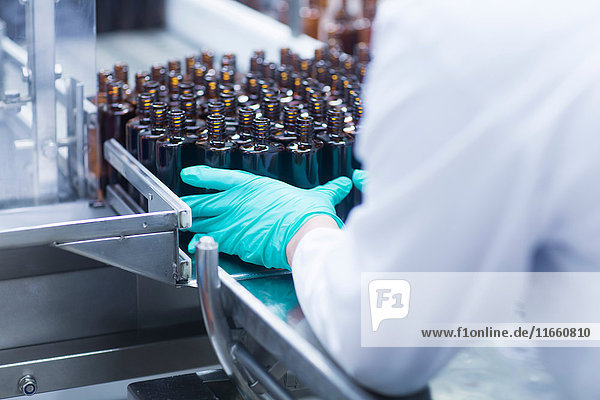 Arbeiter ordnen Flaschen auf einem Förderband in der Produktionslinie einer pharmazeutischen Fabrik an,  mittlerer Abschnitt