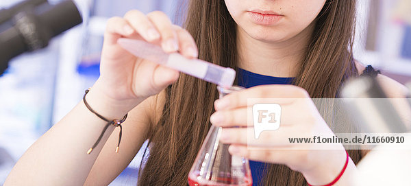 Ein Chemiestudent gießt eine Flüssigkeit in ein Becherglas.