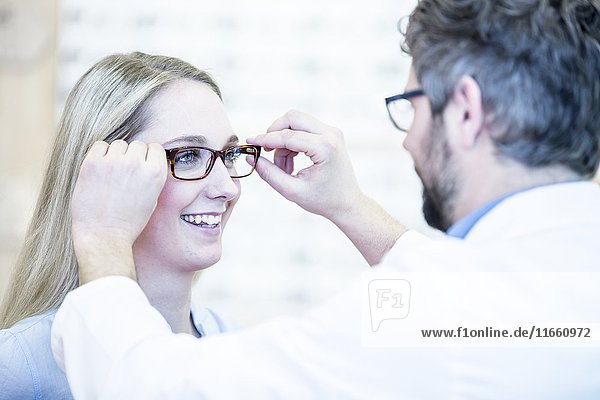 Optikerin probiert eine Brille bei einer Frau im Optikerladen an.