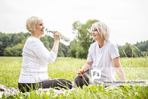 Two women sitting on grass  one drinking water.