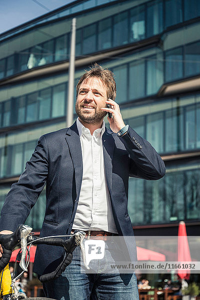 Businessman with bicycle making smartphone call in city