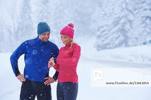 Female and male runners checking smartwatch on deep snow track  Gstaad  Switzerland