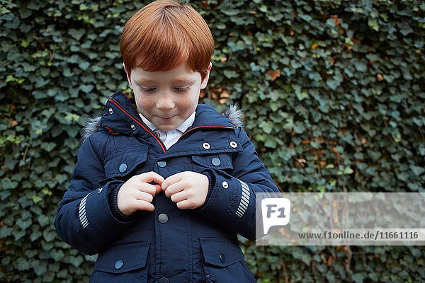 Portrait of red haired boy in front of ivy wall fidgeting with hands