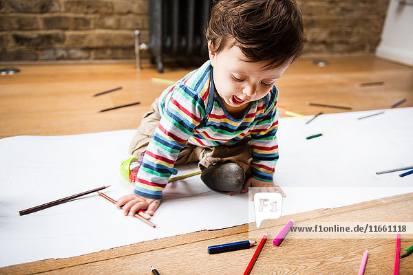 Männliches Kleinkind sitzt auf dem Boden Zeichnung auf langem Papier
