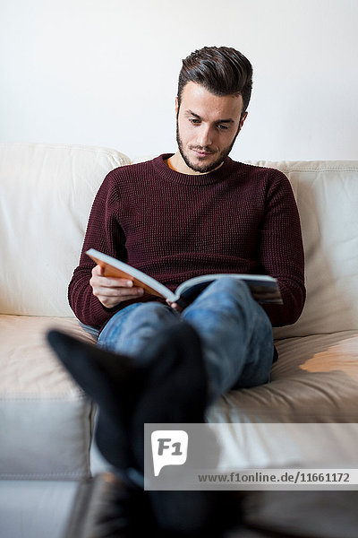 Young man relaxing on sofa reading book