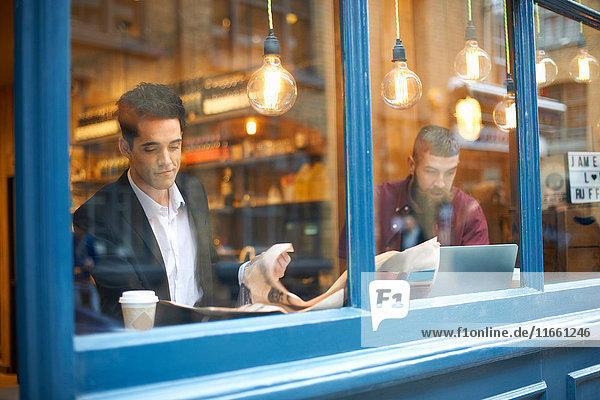 Fensteransicht von Geschäftsleuten  die Zeitung lesen und Laptop im Cafe benutzen