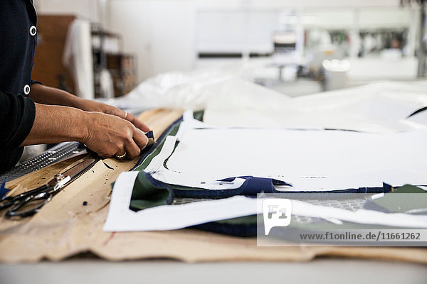 Hände einer Fabrikarbeiterin  die in einer Bekleidungsfabrik ein Schnittmuster für einen Kleidermacher anfertigt