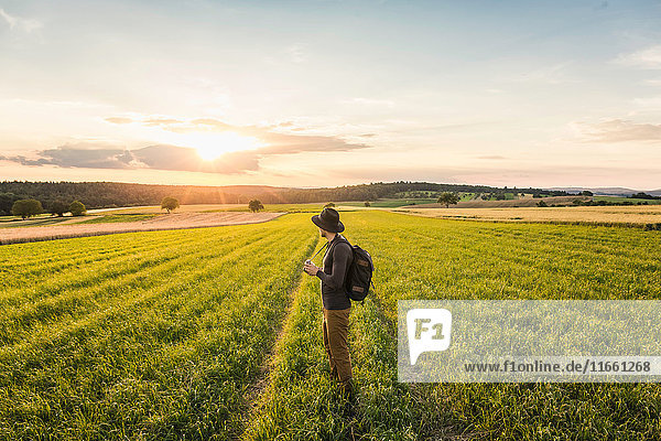 Mid adult man standing in field holding SLR camera looking at view Neulingen Baden-Württemberg Germany
