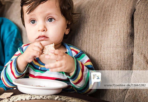 Kleiner Junge sitzt auf dem Sofa  schaut Fernsehen und isst einen Snack