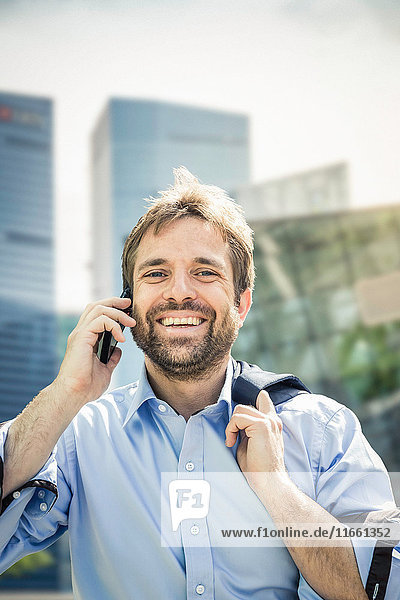 Portrait of happy businessman making smartphone call in city