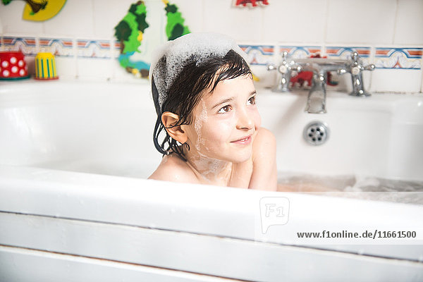 Boy sitting in bath  bubbles on head  smiling
