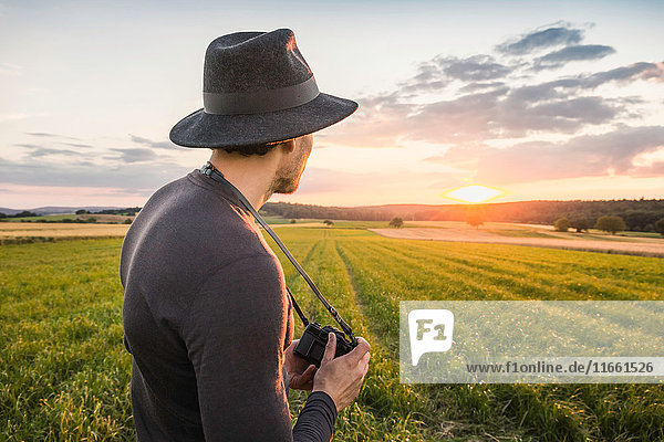 Portrait of mid adult man standing in field holding SLR camera looking at view Neulingen Baden-Württemberg Germany