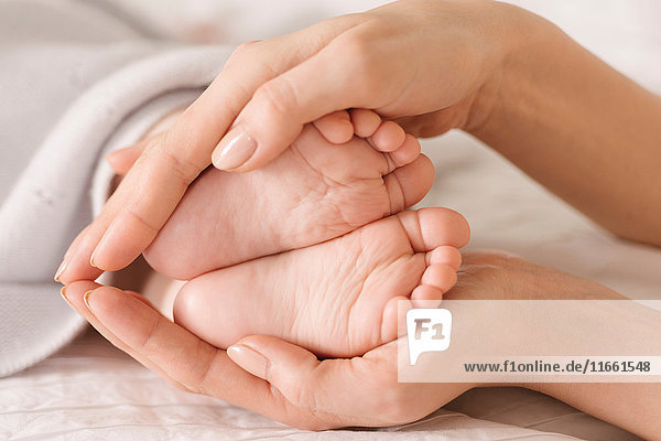 Mother cupping baby's feet on bed