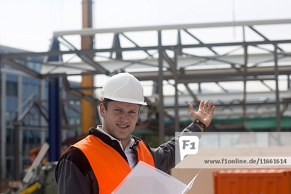 Porträt eines jungen männlichen Bauingenieurs  der auf der Baustelle ein Baugerüst zeigt