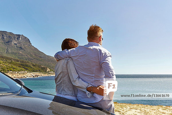 Auf die Motorhaube gelehntes Ehepaar  Blick auf die Küste  Rückansicht  Kapstadt