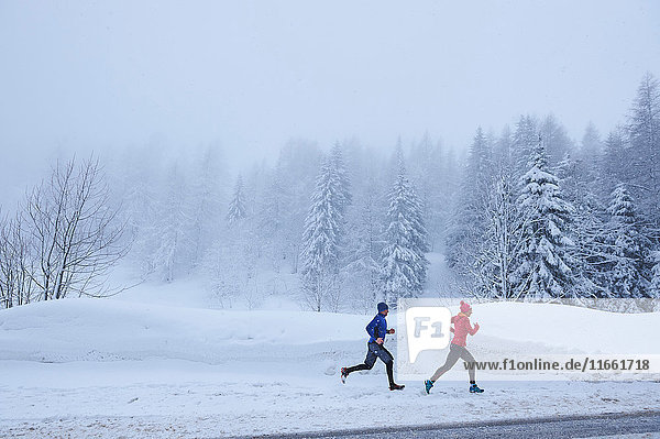 Distant view of female and male runners running in deep snow  Gstaad  Switzerland