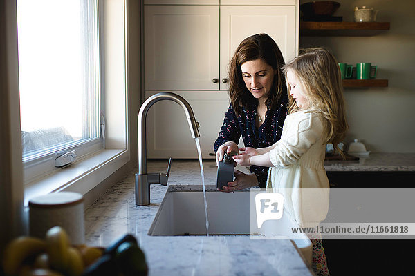 Frau hilft Tochter beim Händewaschen an der Küchenspüle