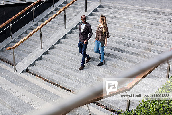 Young businessman and woman moving down city stairway talking