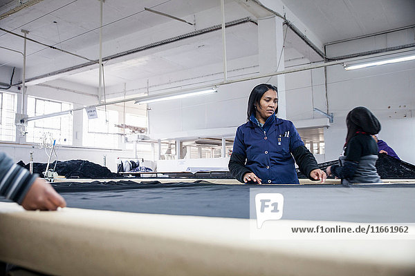 Fabrikarbeiter rollen Textilien auf Arbeitstisch in Bekleidungsfabrik aus