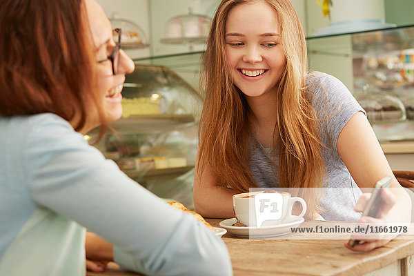 Freunde im Café schauen lächelnd auf das Smartphone