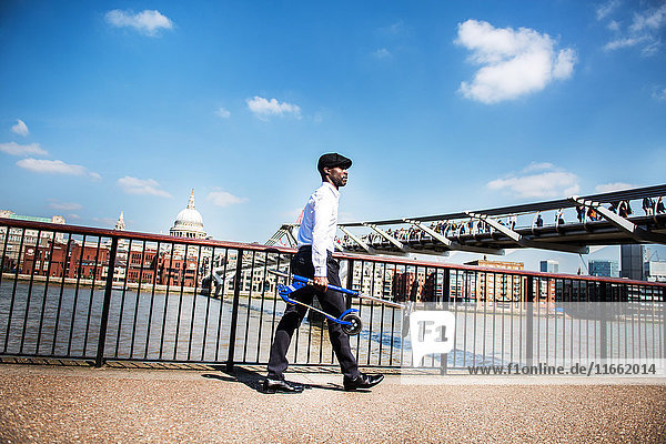 Geschäftsmann mit Roller Millennium Bridge London UK