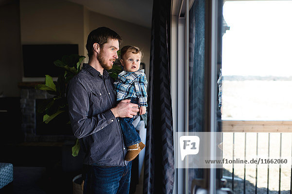 Mann und Kleinkind Sohn schauen zu Hause aus dem Fenster