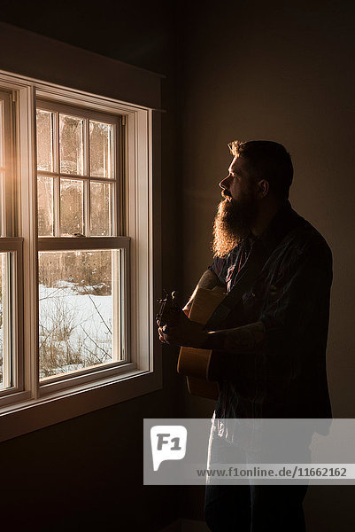Man playing guitar beside window