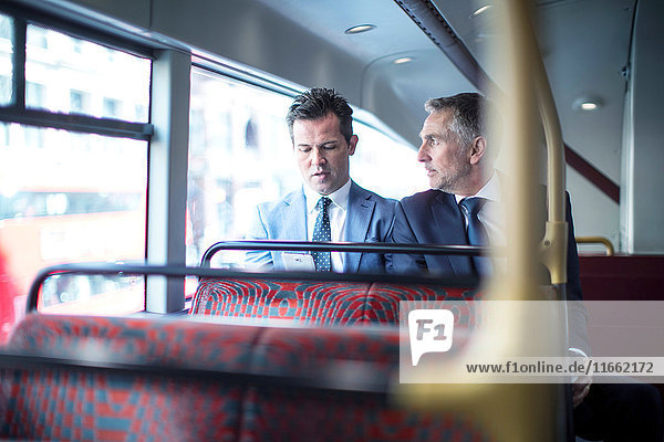 Zwei Geschäftsleute betrachten Smartphone im Doppeldeckerbus
