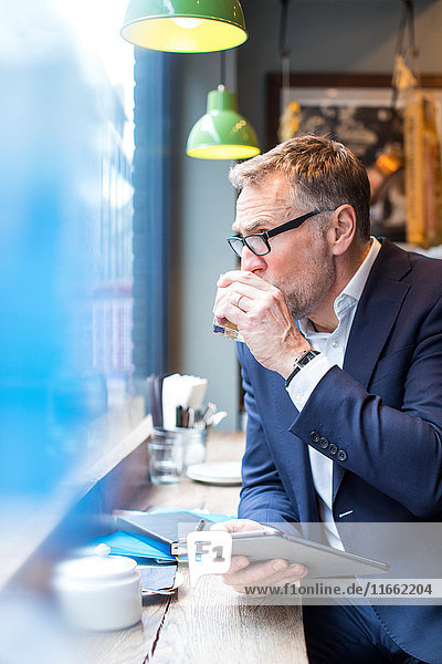 Erwachsener Geschäftsmann mit digitalem Tablett im Restaurant-Fenstersitz