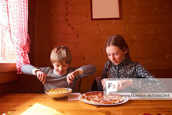 Teenage girl and brother eating pasta and pizza at chalet table