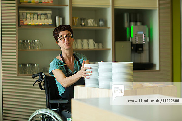 Frau im Rollstuhl  arbeitet im Restaurant  stapelt Schüsseln