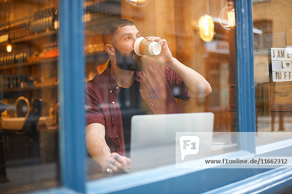 Fensteransicht des jungen Mannes beim Kaffeetrinken im Cafe