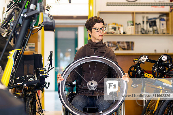Frau im Rollstuhl in Fahrradwerkstatt  die ein Fahrradrad hält