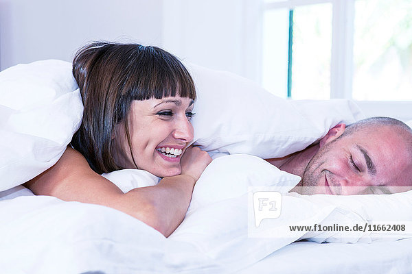 Couple laughing under duvet on bed