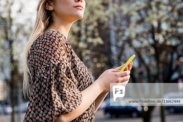 Schnappschuss einer jungen Frau mit Smartphone  die in der Stadt über die Schulter schaut.
