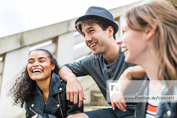 Drei junge erwachsene Freunde auf der Treppe plaudern im Battersea Park