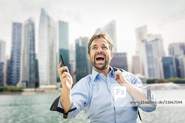 Ecstatic businessman holding smartphone on city waterfront