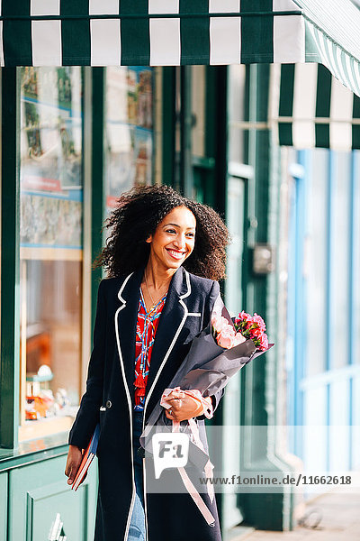 Stilvolle Frau  die mit einem Blumenstrauß die Straße entlang schlendert