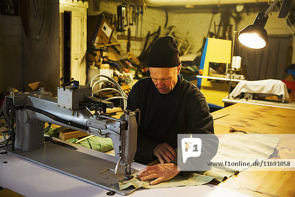 Mann in einer Segelmacherwerkstatt  der mit einer Nähmaschine ein Segel näht.