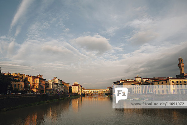 Die Ponte Vecchio und der Arno in Florenz  bei bewölktem Himmel in der Abenddämmerung. Flaches ruhiges Wasser.