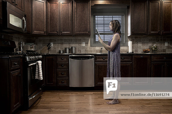 Frau in der Küche bei Nacht  mit digitalem Tablett