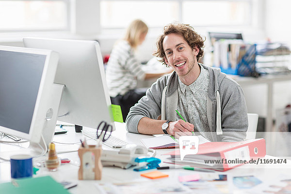 Young man sitting at desk and smiling in creative office  portrait