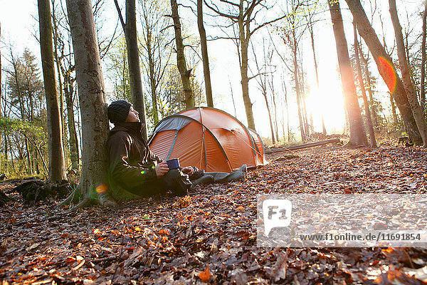 Man drinking coffee by tent in forest