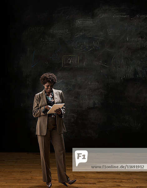 Woman by blackboard using digital tablet
