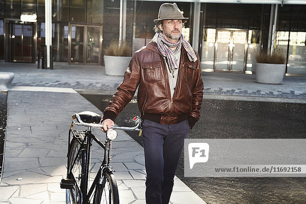 Mittelgroßer erwachsener Mann zu Fuß mit dem Fahrrad in der Stadt