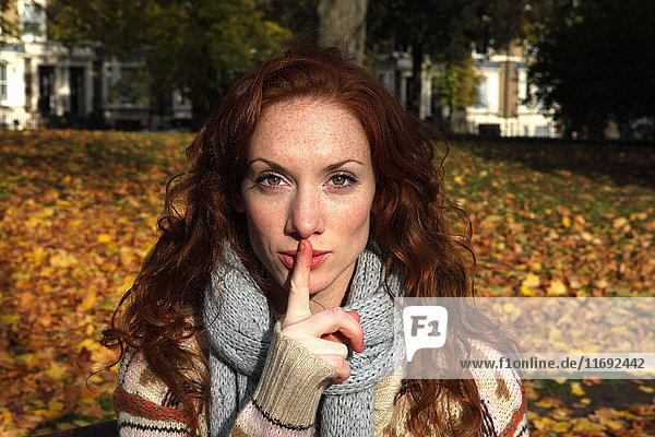 Frau hält im Park den Finger über die Lippen