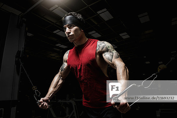 Muskulöser junger Mann  der Pulldown-Übungen im Fitnessstudio ausführt