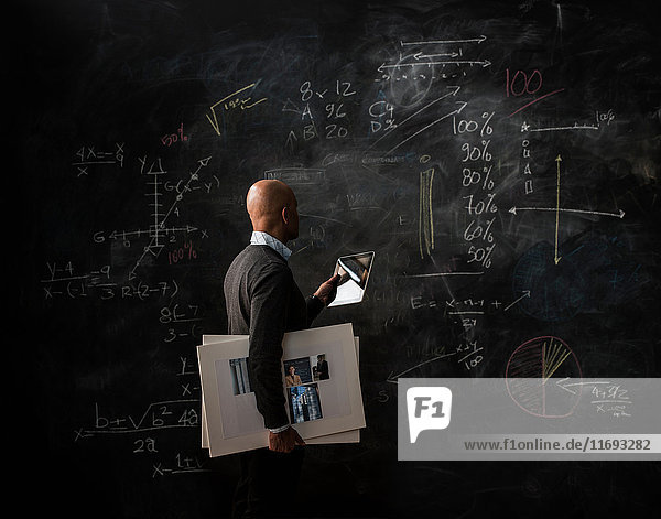 Businessman by blackboard with digital tablet and moodboard