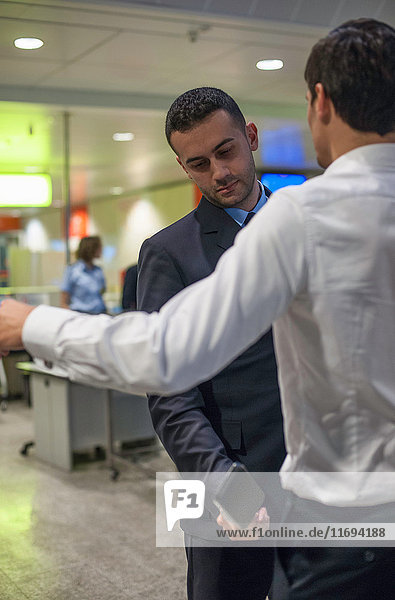 Wachmann kontrolliert männlichen Passagier bei der Flughafensicherheit