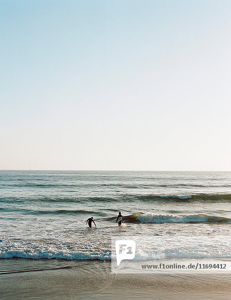 Surfer  die am Strand in Wellen laufen
